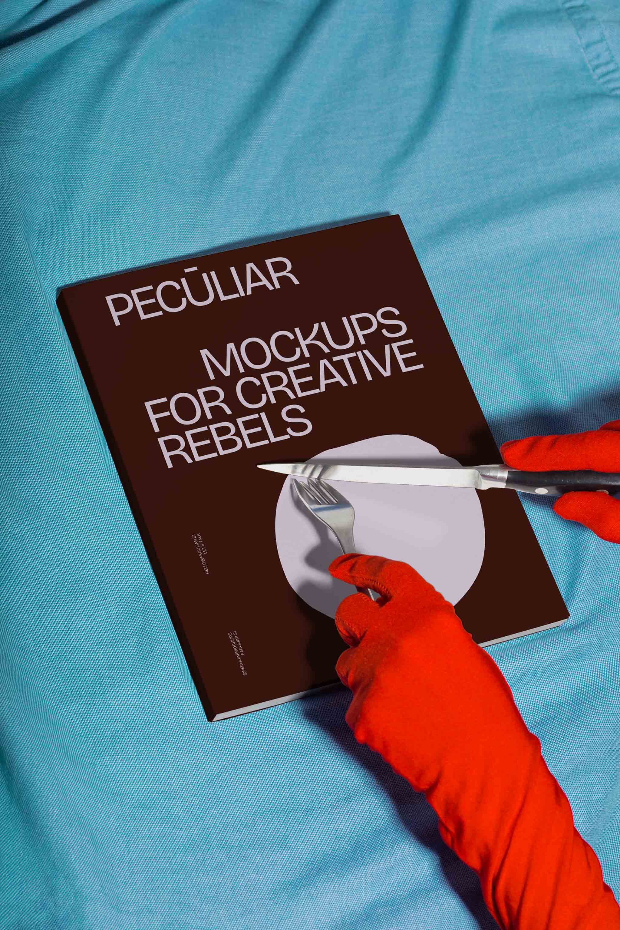 Two gloved hands holding utensils over a book cover mockup set against blue fabric, in use example.