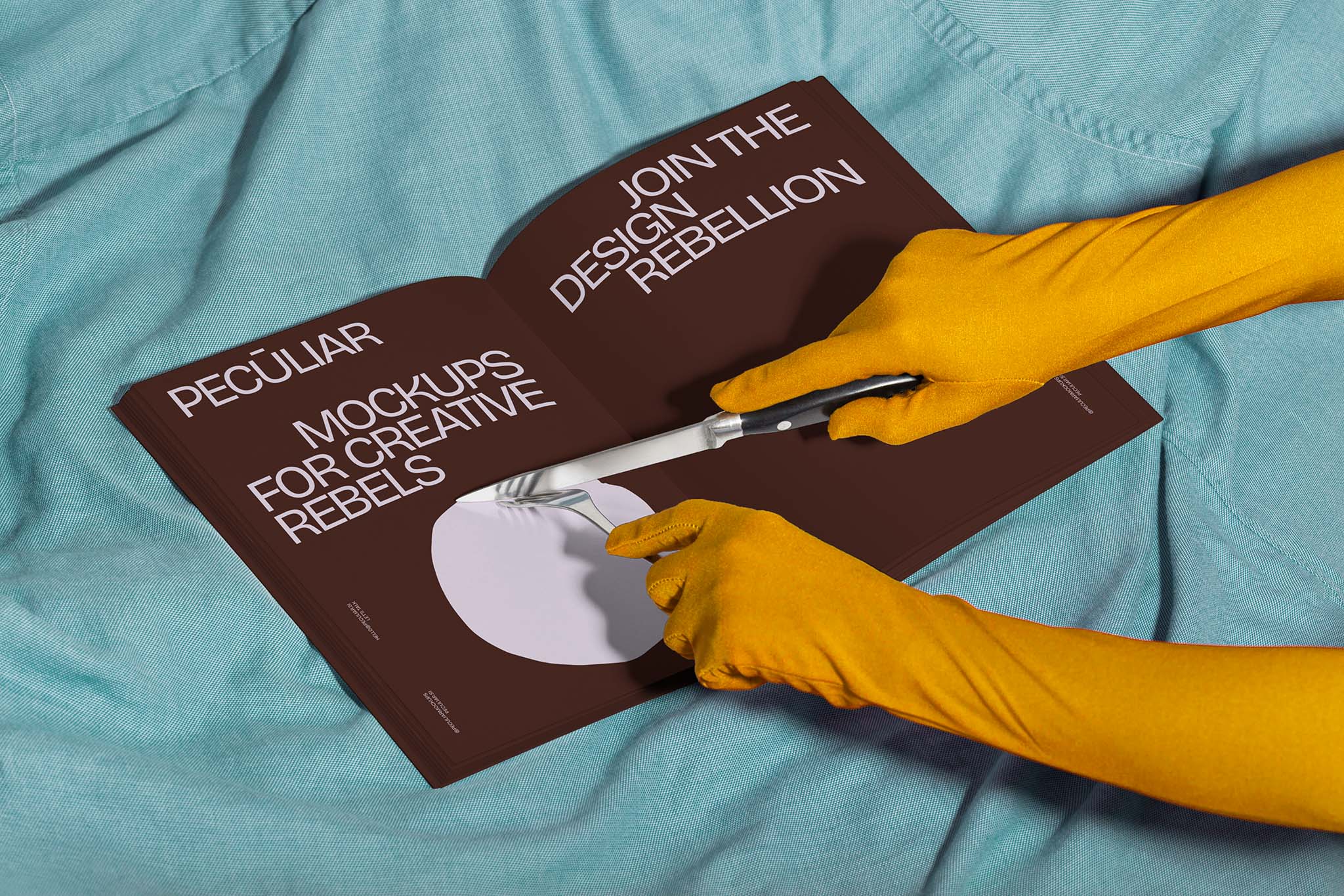 Two gloved hands holding utensils over an open book mockup set against light blue fabric, in use example.