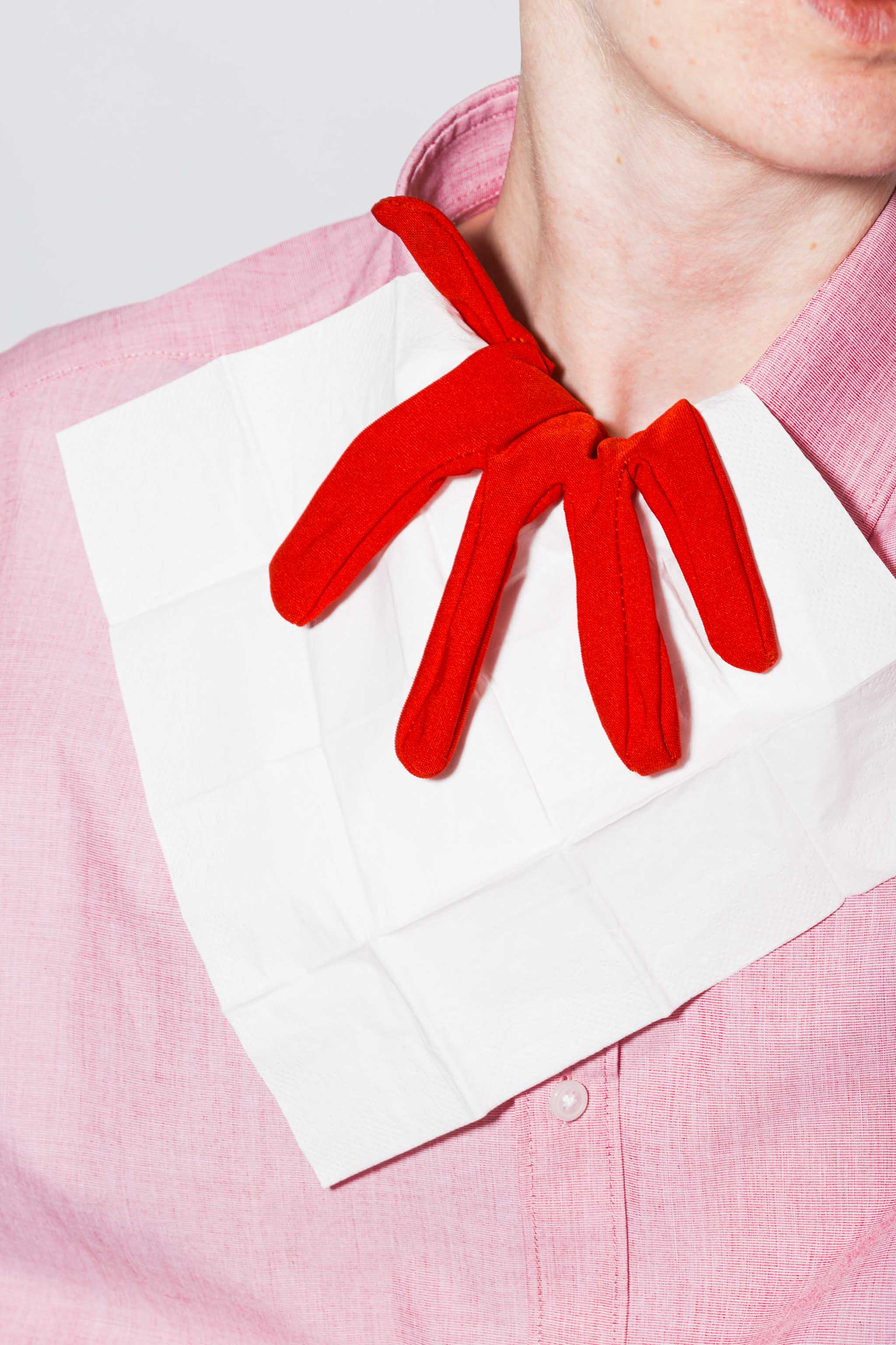 Close-up photo of a person in a pink dress shirt on top of which a white napkin print mockup with black lettering and a red glove are tucked, empty mockup.