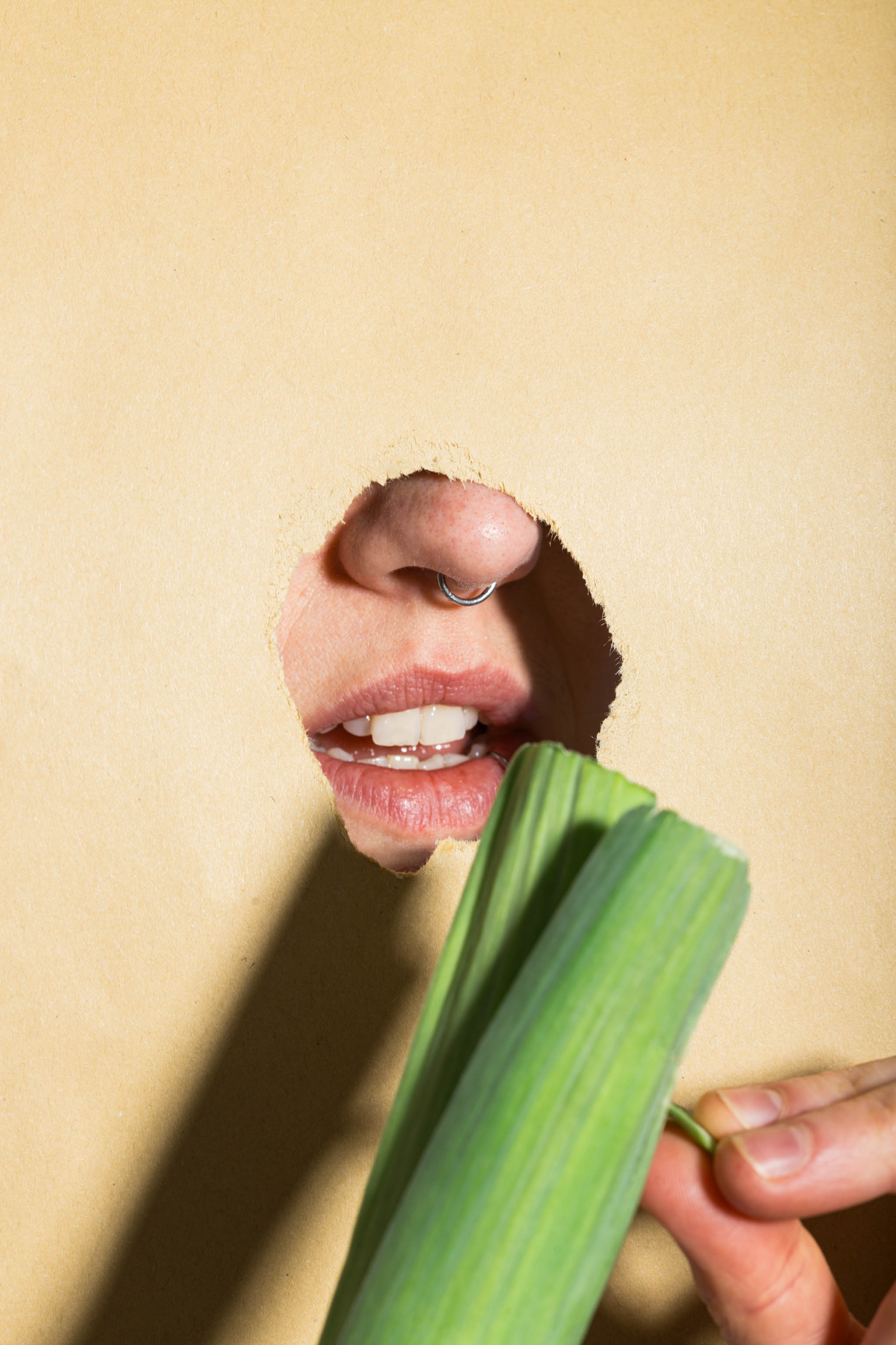 Close-up photo of a torn poster mockup with black typographic print placed on top of a person's mouth while they're peeling a raw leek, empty mockup.