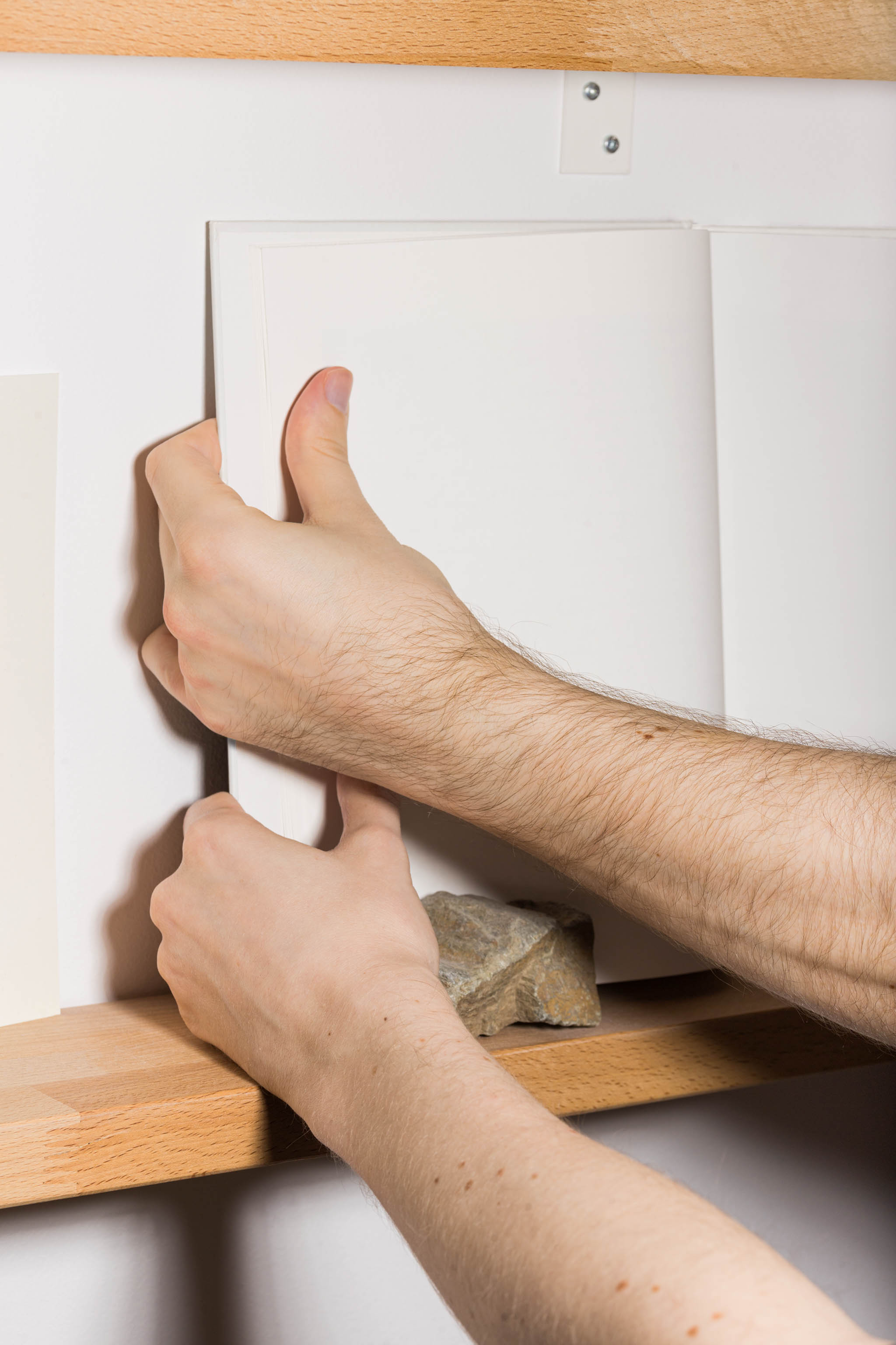 Two hands holding an open book mockup on wooden bookshelves, empty mockup.