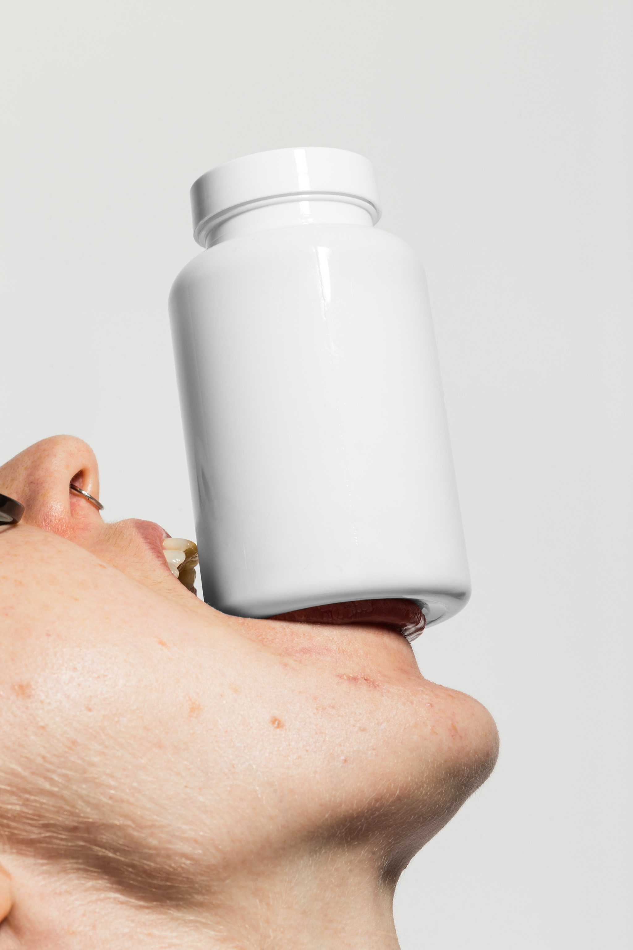 Close-up mockup of a person's face holding up a pill bottle with their mouth, empty mockup.