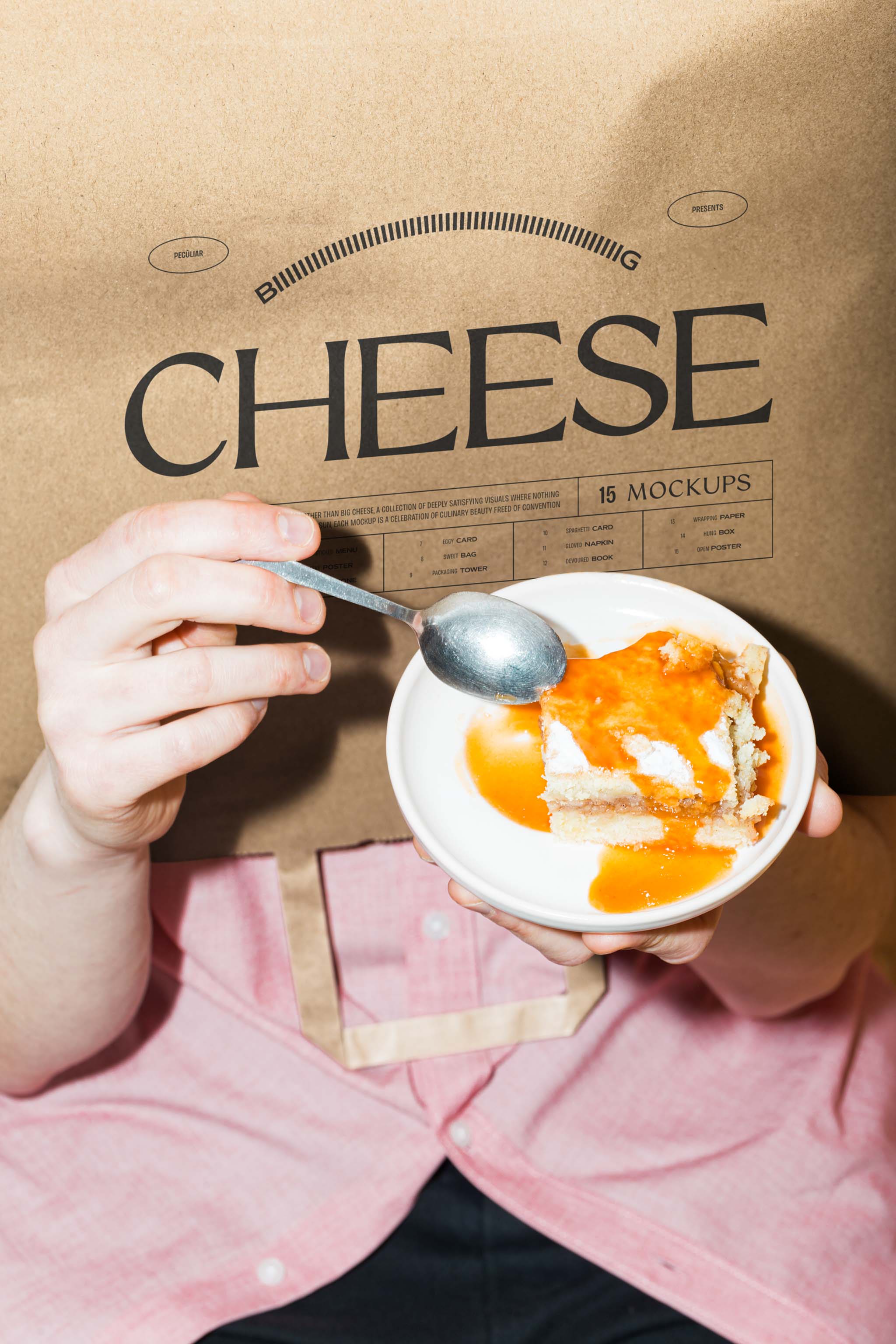 Close-up photo of paper bag mockup turned upside-down over a person's head while they're holding up a sweet orange dessert in a pink dress shirt and black pants, in use example.