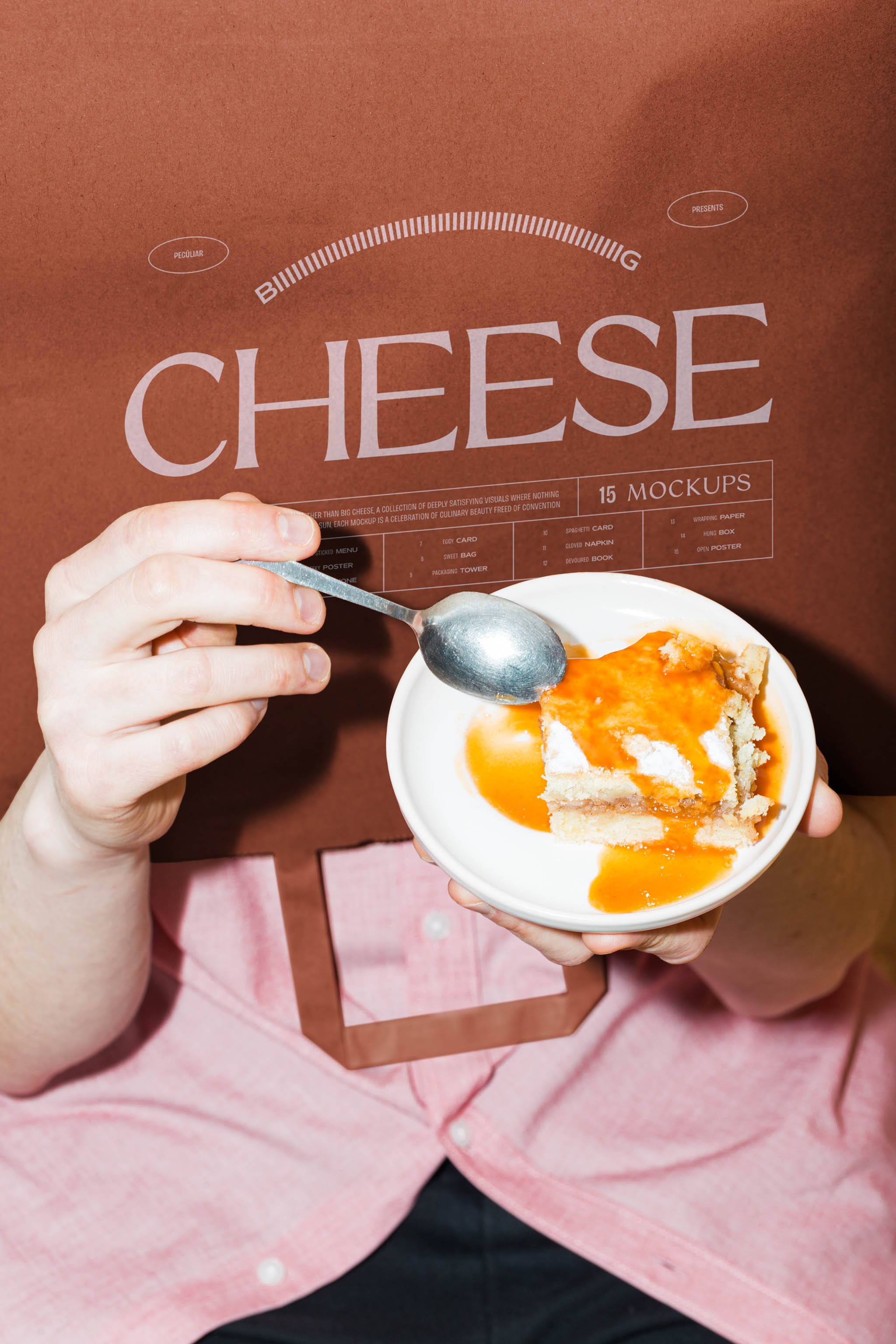 Close-up photo of paper bag mockup turned upside-down over a person's head while they're holding up a sweet orange dessert in a pink dress shirt and black pants, in use example alternative colors.