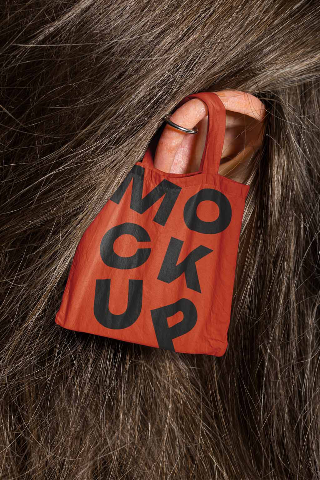 Canvas tote bag mockup hung on a person's ear amid dark wavy hair, alternative version.